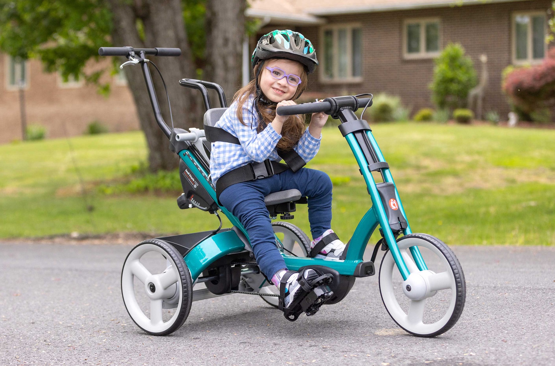 A girl rides on a small teal Rifton Adaptive Tricycle.