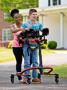 Using a standard base on the Rifton Dynamic Pacer, a client walks with his caretaker on a black top road.