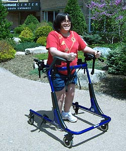 A smiling woman in a Rifton gait trainer (a device designed to offer more support than a typical quad walker) practices forward movement on four wheels.