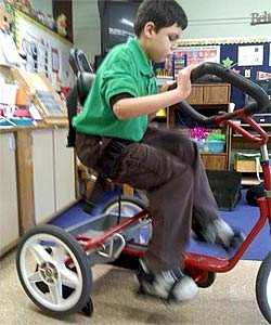 A young boy exercising on his adaptive tricycle in the classroom thanks to the Rifton stationary bike stand.