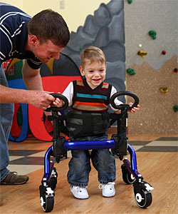 A toddler, with the help of a therapist, practices control in a gait trainer while learning functional motor skills 