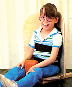 A young girl with glasses in a corner floor sitter smiles as she tests the product for improvements