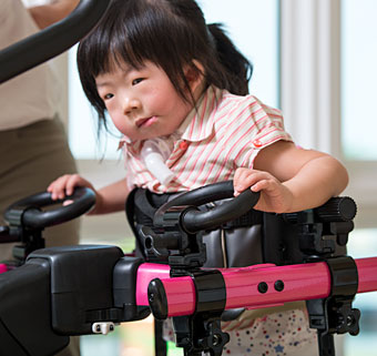 A young girl with a neurological condition uses a gait trainer to assist in walking