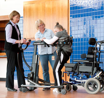 Two caregivers perform a patient wheelchair to stand transfer using the TRAM- a safe patient handling device.