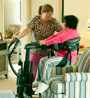 A caregiver transfers a patient from the couch to the wheelchair using safe patient handling equipment.