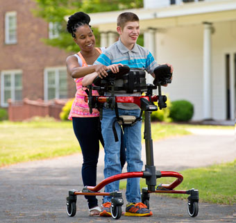A caregiver assists a teenager using a medically necessary dynamic gait trainer outdoors