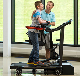 A young man get assistance from a therapist as he practices treadmill gait training inside a rehab clinic