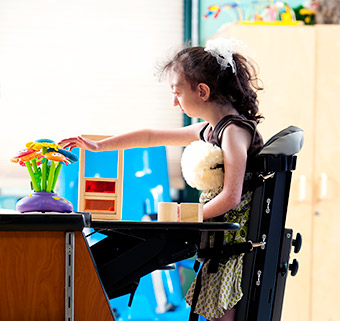 A young girl feels flowers on a table while standing in a Rifton Mobile Stander.