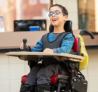 A portrait of a boy sitting in his red Rifton Activity Chair and smiling.
