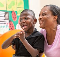 A boy and caregiver in a classroom smile at the camera.