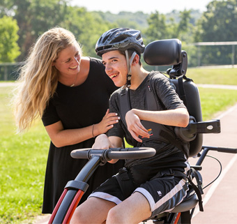 A young man on a Rifton Adaptive Trike smiles with his caregiver