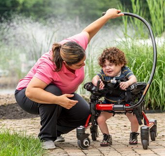 A little boy walks in a Rifton Pacer gait trainer while his caretaker assists him.