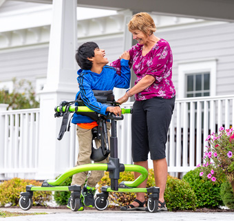 A boy walks in a Rifton Pacer while his caretaker talks with him.