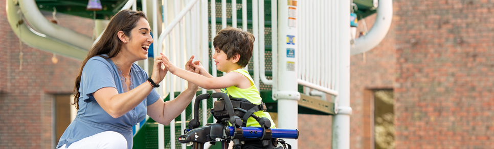 A physical therapist talking to a boy in a Rifton Pacer.