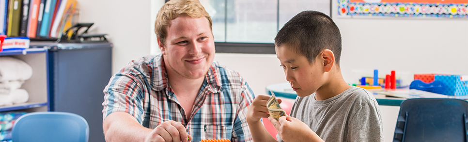 A boy and a young man look at a dollar bill.