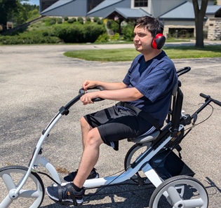 A young man rides on a white Rifton Adaptive Tricycle.