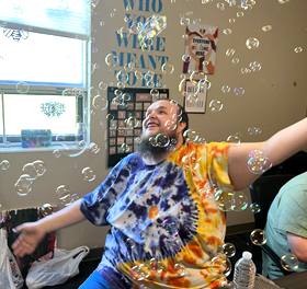 A man with disabilities blows bubbles and smiles.