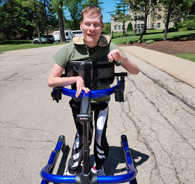 A young man walks down a road using a Rifton Pacer gait trainer.