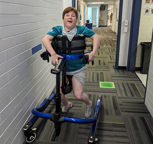 A young woman walks with the help of a Rifton Pacer gait trainer.