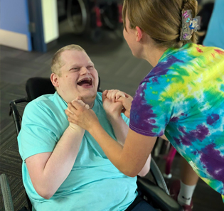 A young man holds the hands of a young woman and smiles at her.