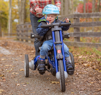 A boy rides a blue Rifton Adaptive Tricycle on a mountain trail.