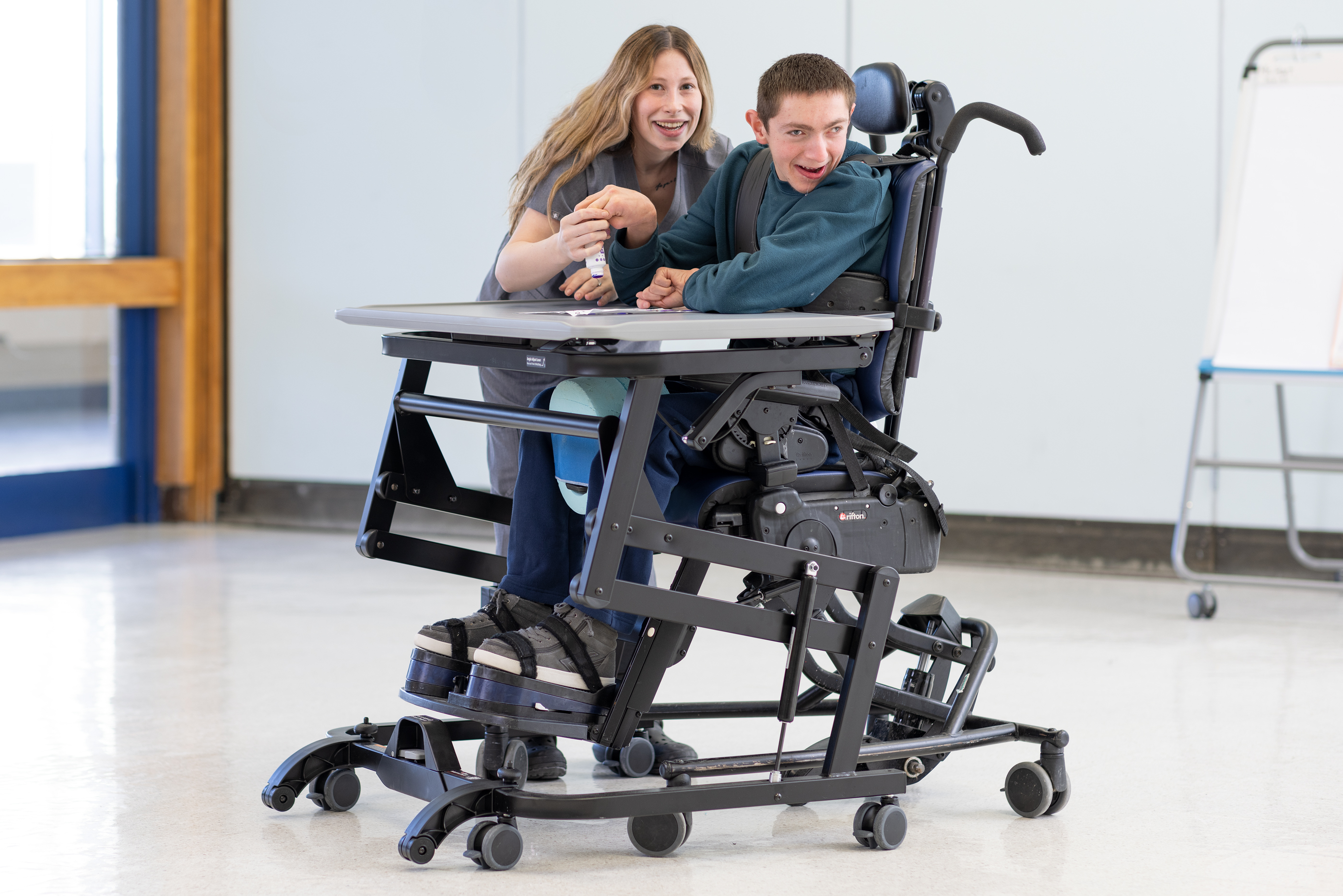 A young man sits in a Rifton Activity Chair at a Rifton Adaptive Desk.