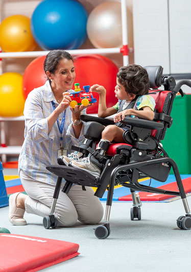 A boy sits in a Rifton Activity Chair and plays with a toy train with his therapist.