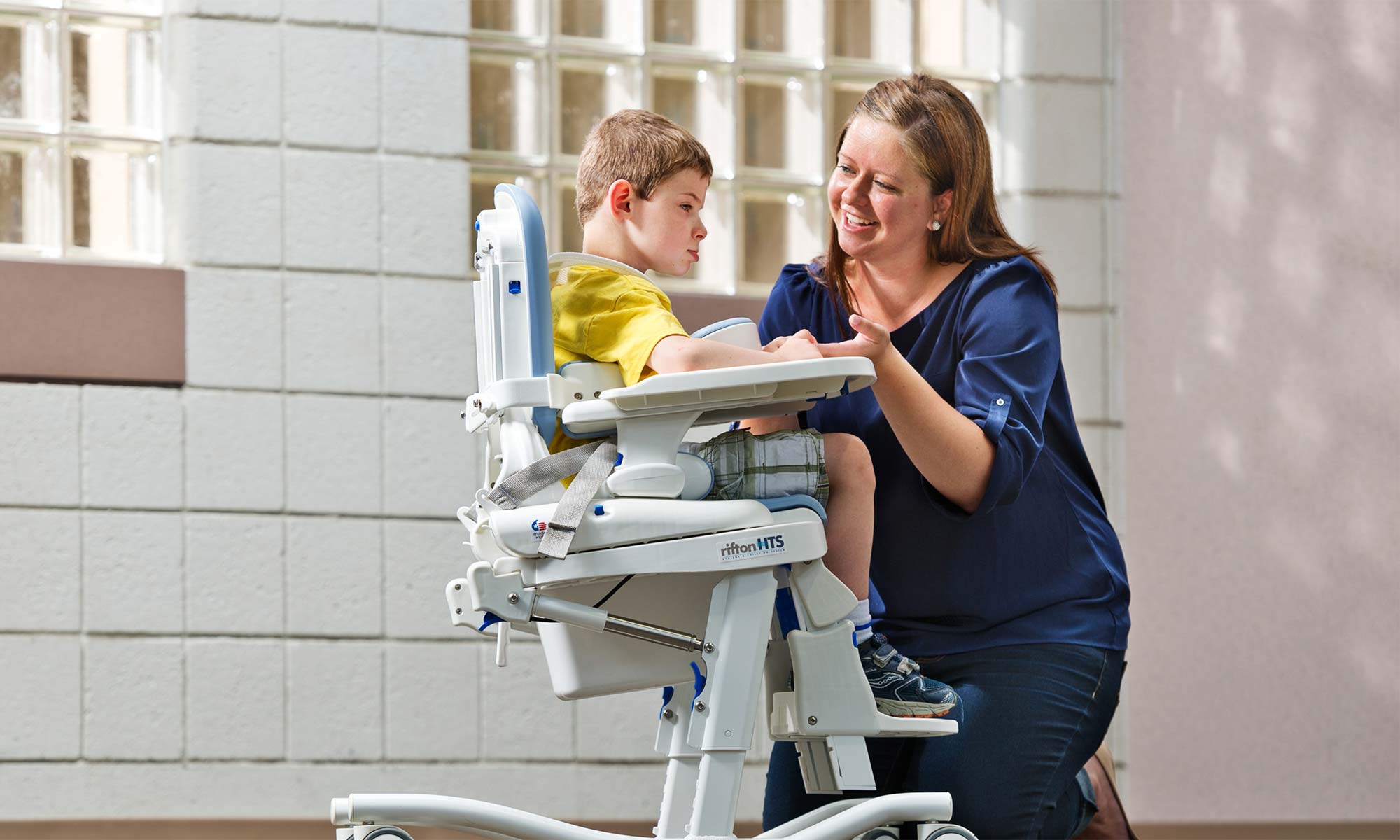 A boy sits in a Rifton HTS (Hygiene and Toileting System) and talks with his caregiver.