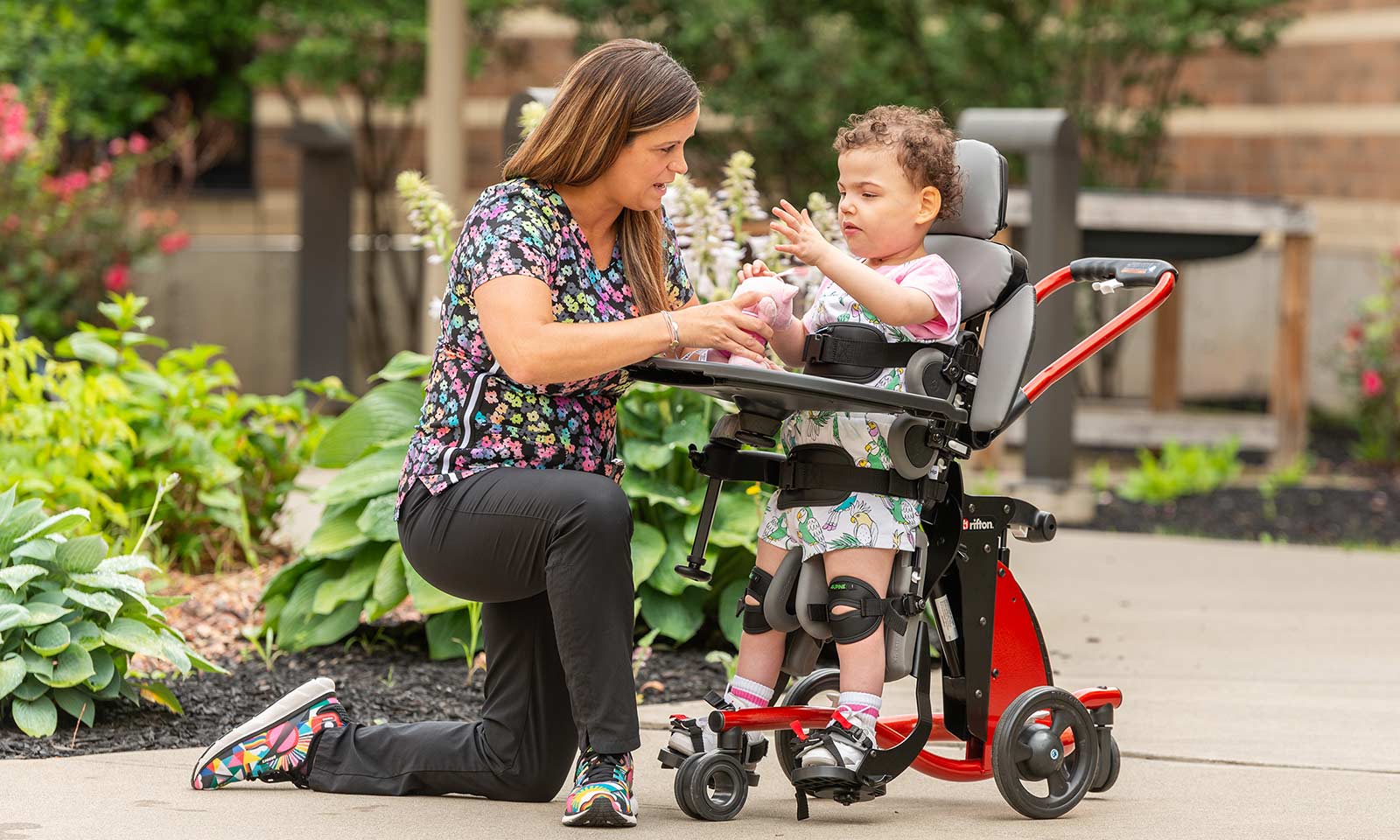 A girl uses Rifton Standing Frame to play with a toy with her caretaker.