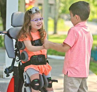 A young girl in a size 1 Rifton supine stander holds hands with her brother.