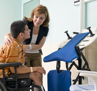 A young man, assisted by a caregiver, using a Rifton Support Station
